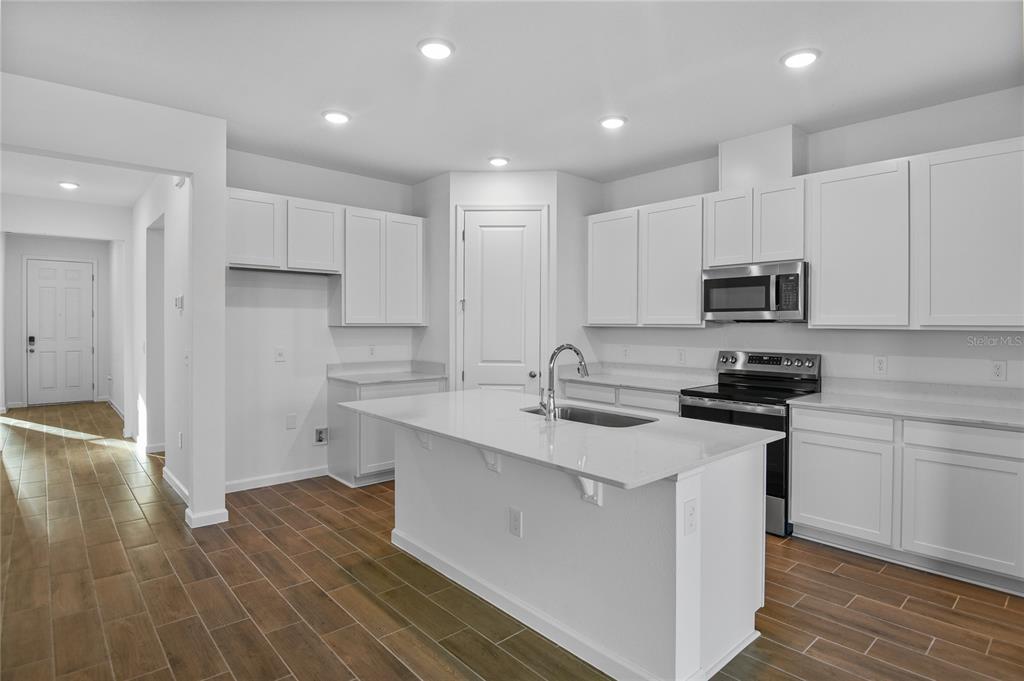 A modern kitchen features white cabinets, a central island with a sink, and wood-look flooring — 6179 DAPHNE STREET, LAKE HAMILTON, FL