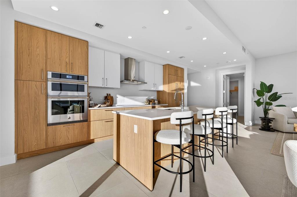 A modern kitchen features light wood cabinetry, white upper cabinets, a central island, and barstools — 275 1ST AVE S UNIT 2706, ST PETERSBURG, FL