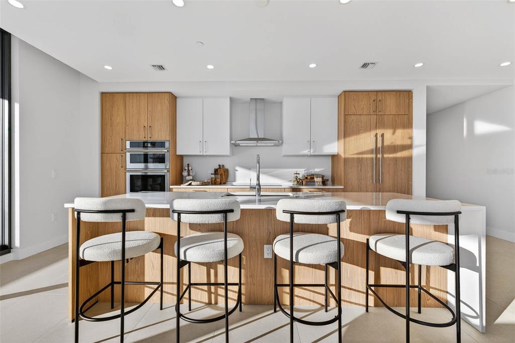 A modern kitchen features a large island with four stools, wood cabinetry, and white upper cabinets — 275 1ST AVE S UNIT 2706, ST PETERSBURG, FL