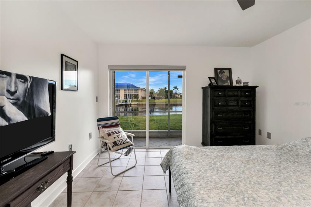 A bedroom features tile flooring, a television, a dresser, and a sliding door to a patio — 311 GARVIN STREET UNIT 205A, PUNTA GORDA, FL