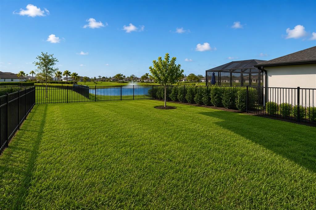 A fenced backyard features a green lawn, a small tree, and a view of a pond — 17809 BELFORTE COURT, NORTH FORT MYERS, FL