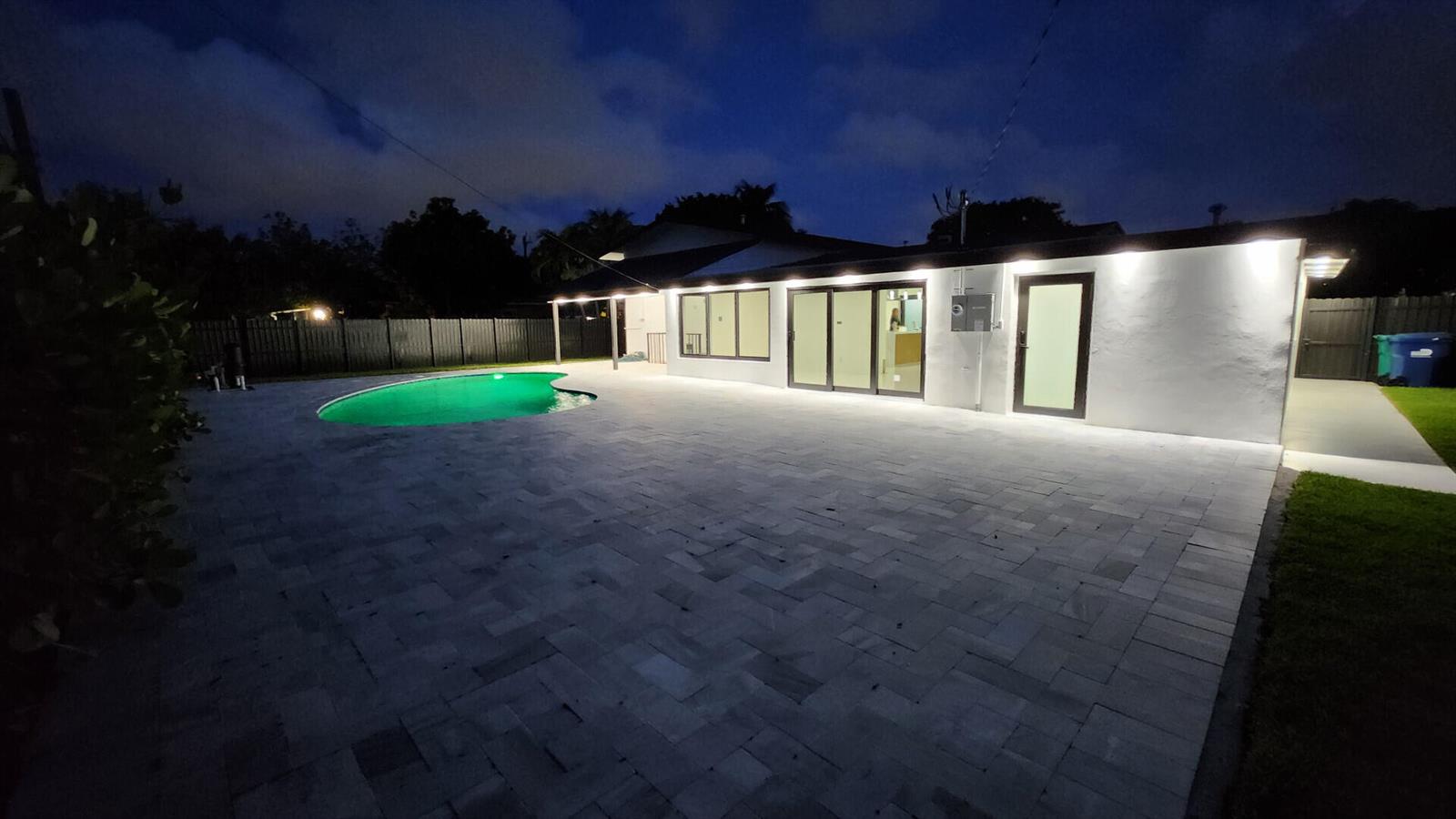 A backyard at night featuring a paved patio, a lit swimming pool, and a white house — 1275 NE 200th Terrace, Miami FL 33179, MIAMI, FL