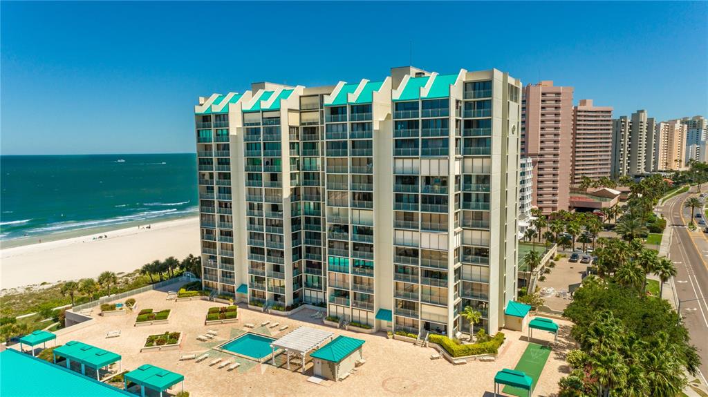 An aerial view of a tall beachfront condominium building with a pool and patio area — 1380 GULF BOULEVARD UNIT 307, CLEARWATER BEACH, FL