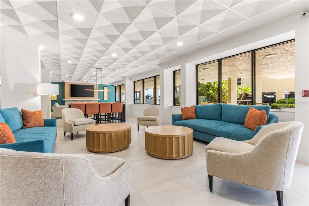 A modern lounge area features blue sofas, beige armchairs, round wooden tables, and a textured ceiling — 1380 GULF BOULEVARD UNIT 307, CLEARWATER BEACH, FL