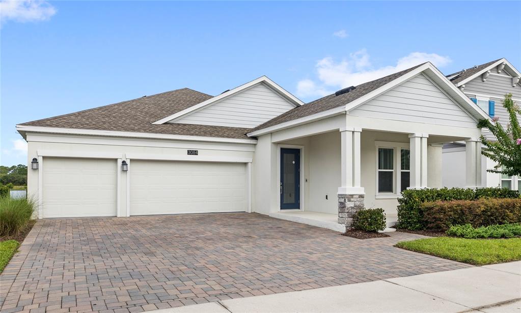 A single-story house with a three-car garage, stone-accented porch, and a paved driveway — 3084 ELLA WAY, ST CLOUD, FL