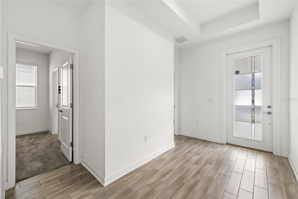 An entryway features wood-look tile flooring, white walls, and a front door with glass panels — 3084 ELLA WAY, ST CLOUD, FL