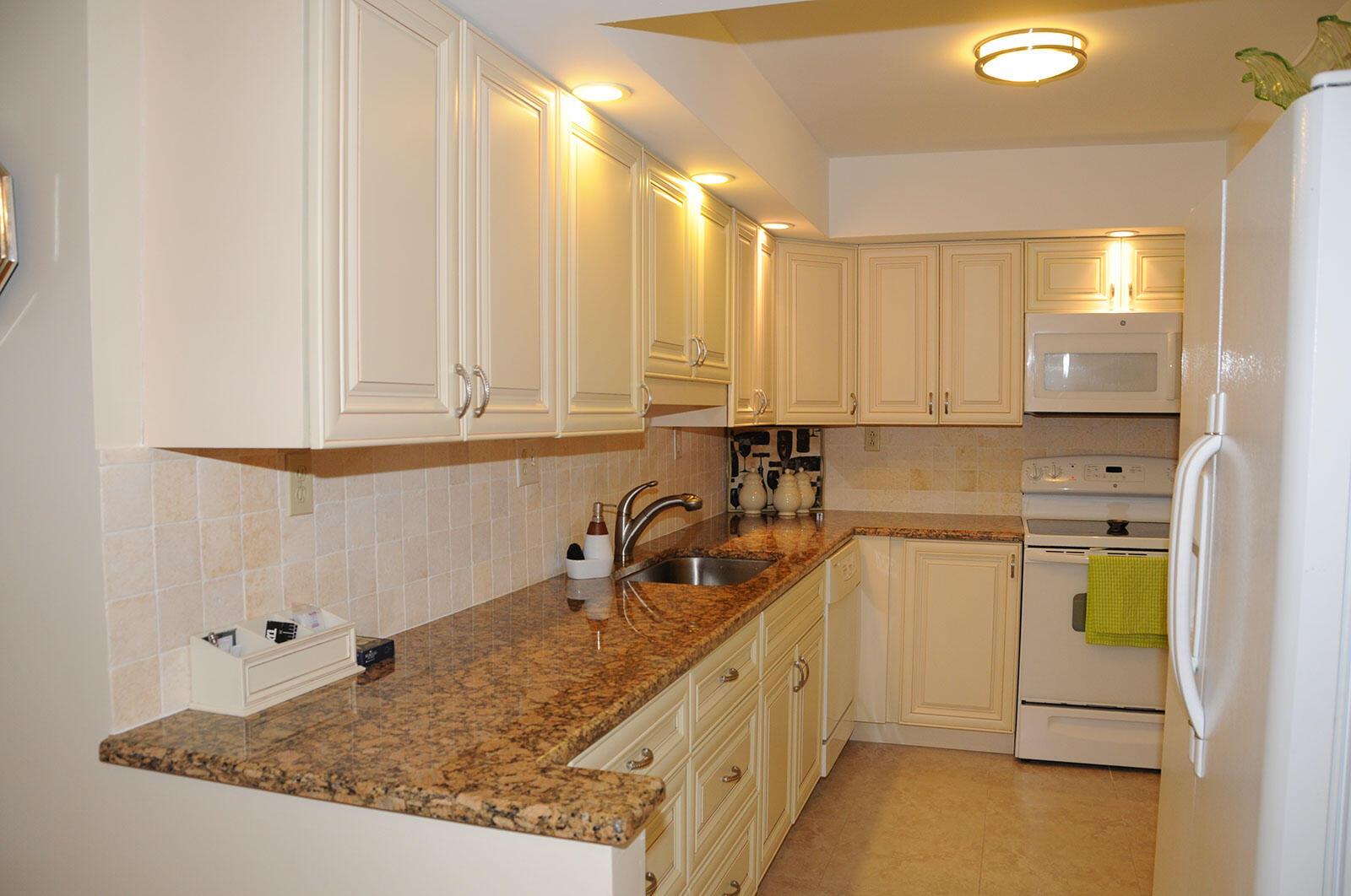 A kitchen with cream cabinets, granite countertops, tile backsplash, and white appliances — 525 N Ocean Boulevard # 1120, Pompano Beach FL 33062, POMPANO BEACH, FL