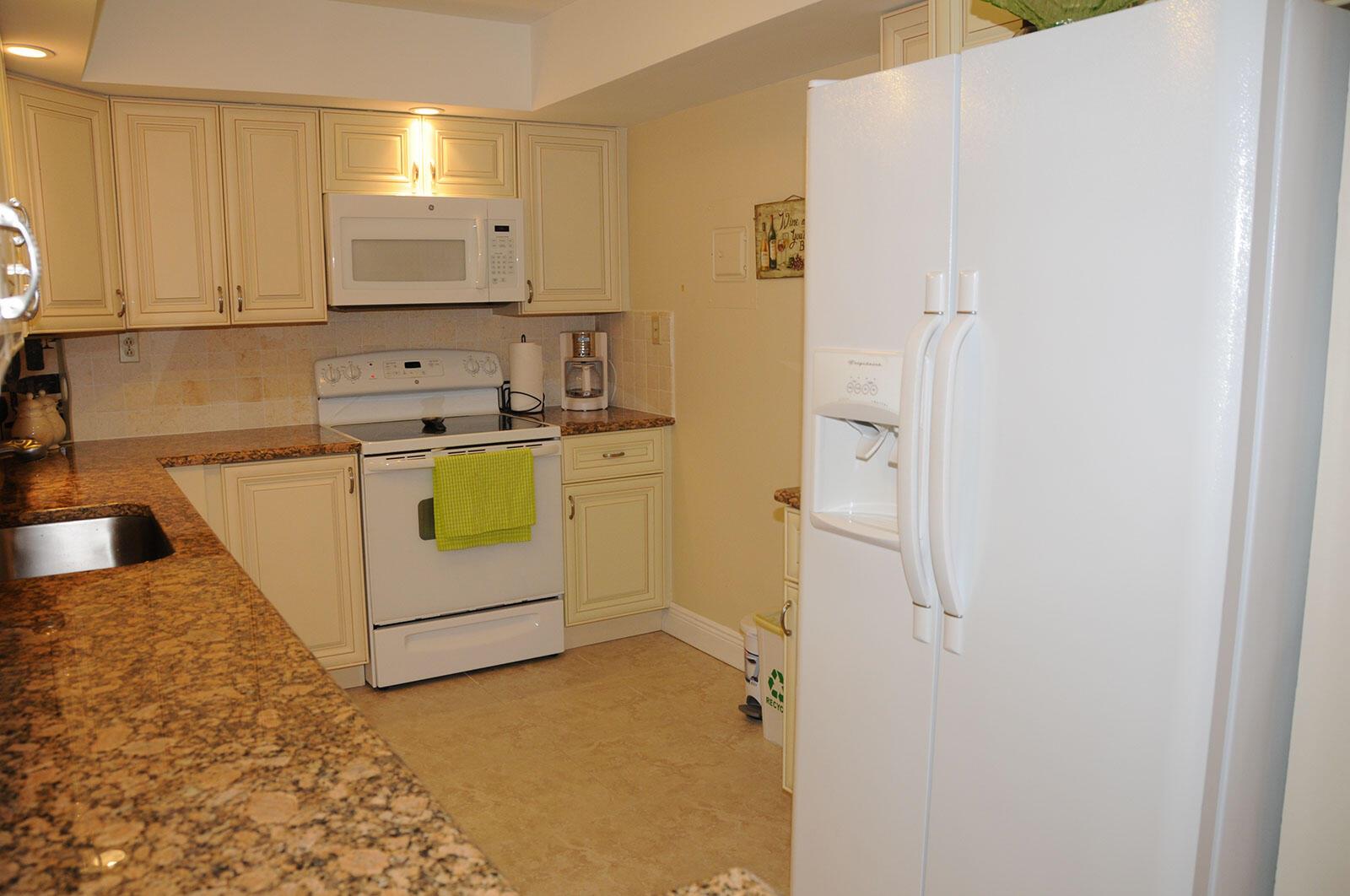 A kitchen with cream-colored cabinets, granite countertops, white appliances, and a tile floor — 525 N Ocean Boulevard # 1120, Pompano Beach FL 33062, POMPANO BEACH, FL