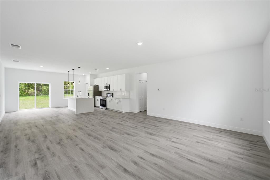 An open-concept kitchen and living area features white cabinetry, stainless appliances, and gray wood flooring — 16390 SW 27TH TERRACE ROAD, OCALA, FL