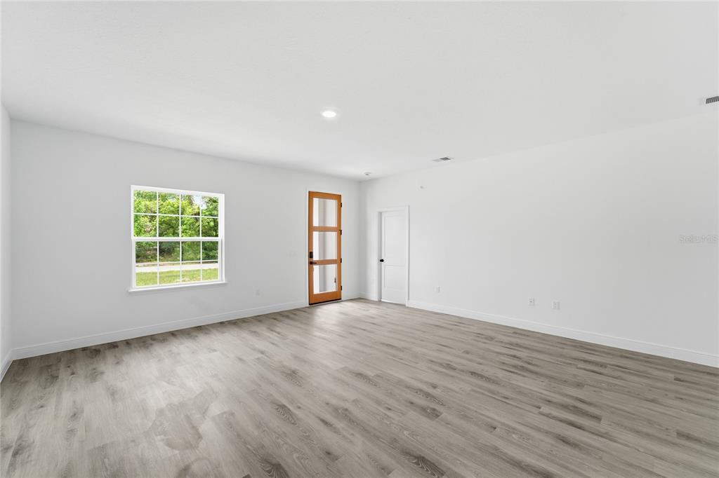 An empty room with white walls, wood-look flooring, a window, and a wooden door — 16390 SW 27TH TERRACE ROAD, OCALA, FL