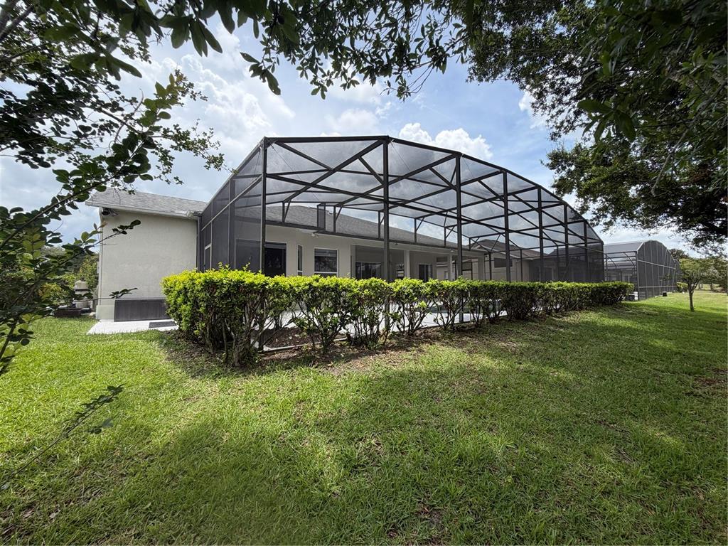 A backyard view of a house with a large screened-in pool enclosure and hedges — 2734 WINDSORGATE LANE, ORLANDO, FL