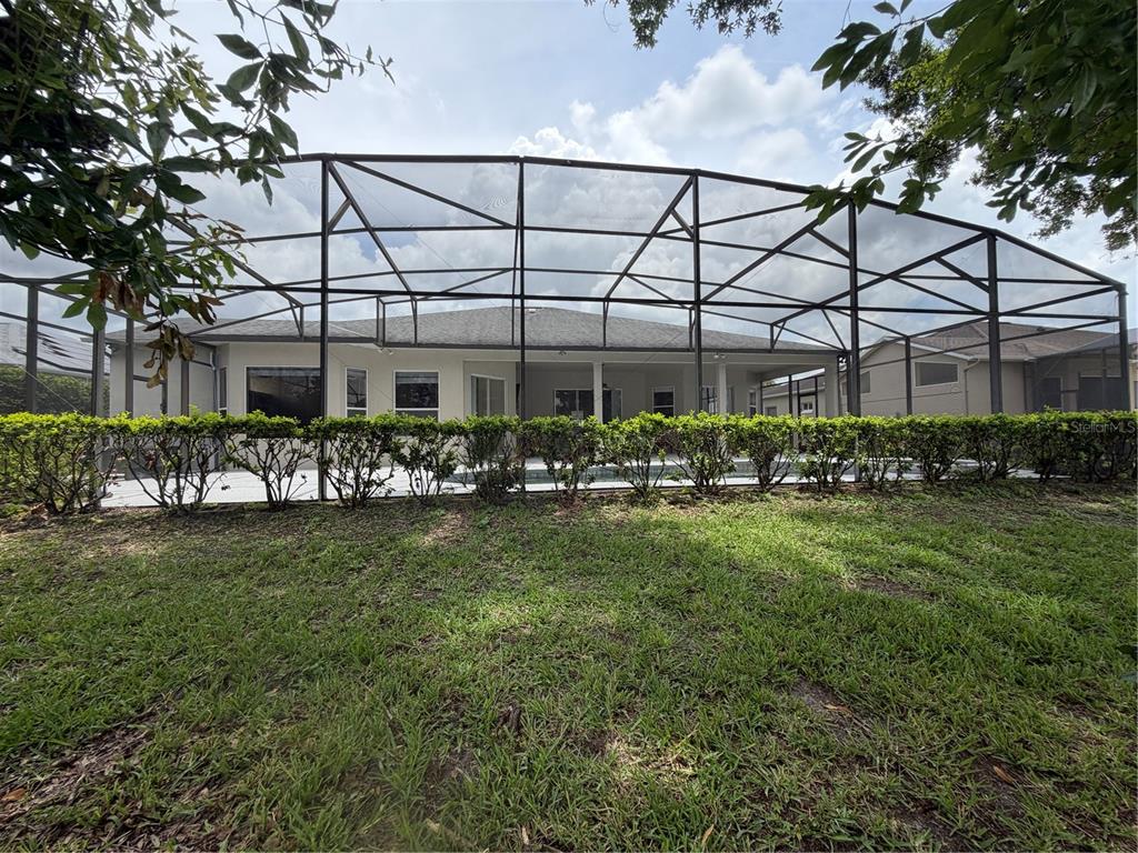 A backyard view of a house with a screened-in pool enclosure and a hedge — 2734 WINDSORGATE LANE, ORLANDO, FL