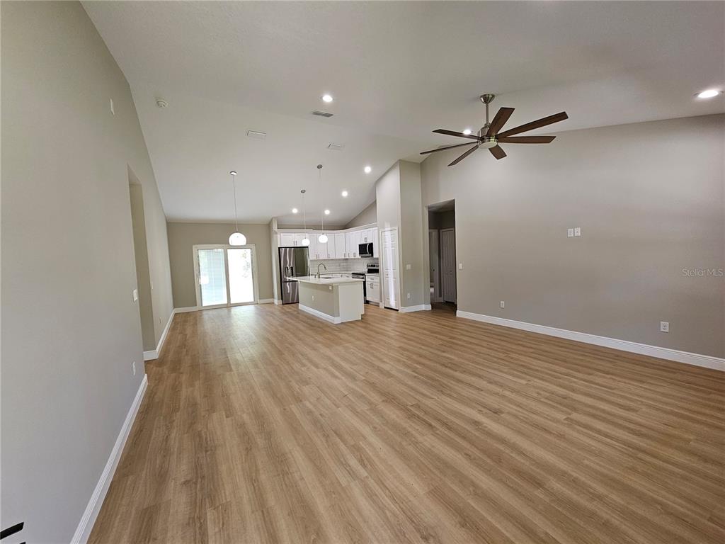 An open-concept living area features light wood-look flooring, a kitchen island, and vaulted ceilings — 6920 SE 123RD PLACE, BELLEVIEW, FL