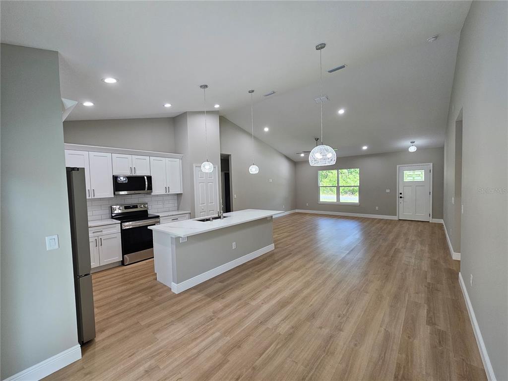 An open-concept kitchen and living area features white cabinets, a central island, and wood-look flooring — 6920 SE 123RD PLACE, BELLEVIEW, FL