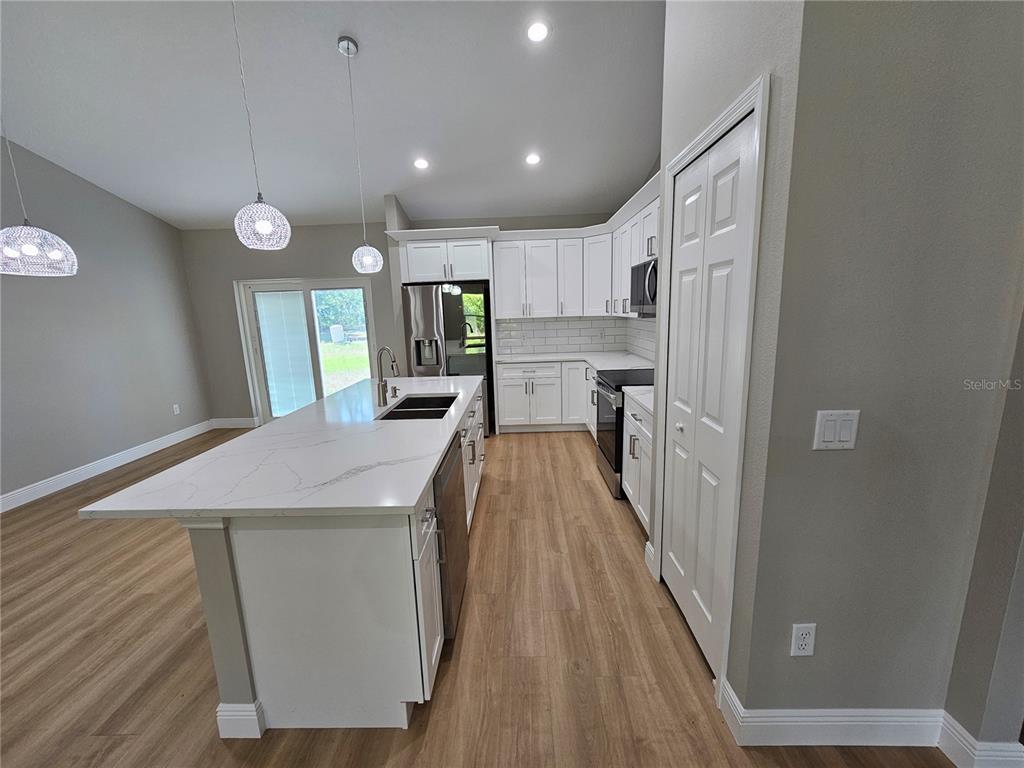 A modern kitchen features white cabinetry, a quartz-topped island, and light wood-look flooring — 6920 SE 123RD PLACE, BELLEVIEW, FL