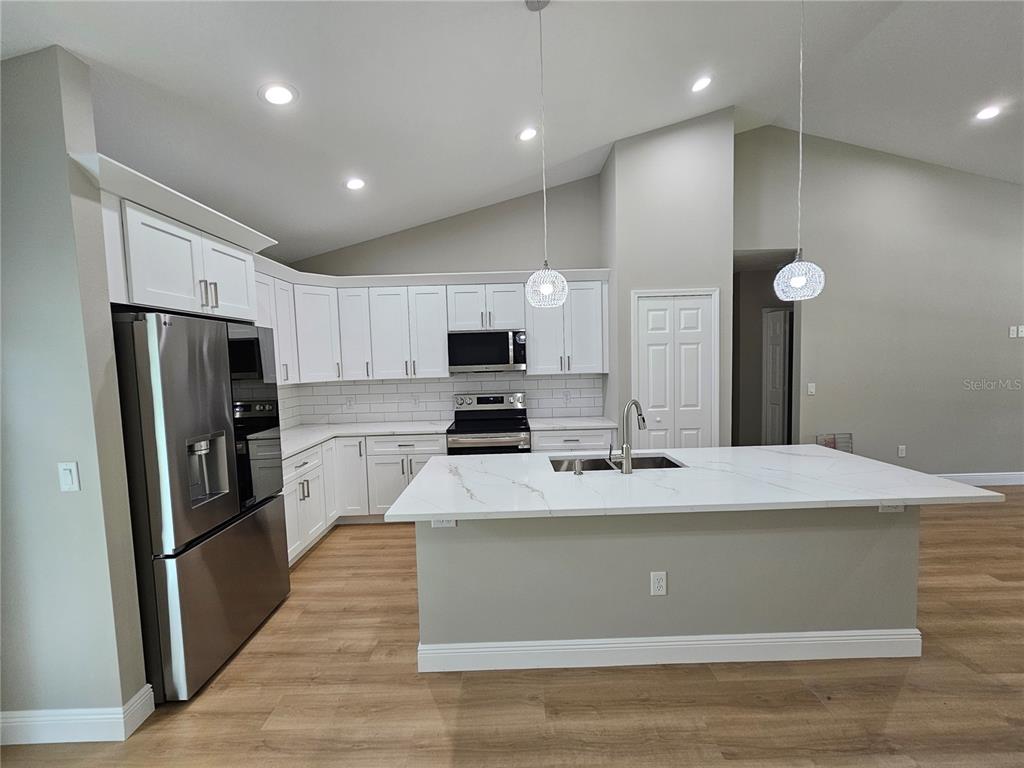A modern kitchen features white cabinets, stainless steel appliances, and a marble-topped center island — 6920 SE 123RD PLACE, BELLEVIEW, FL