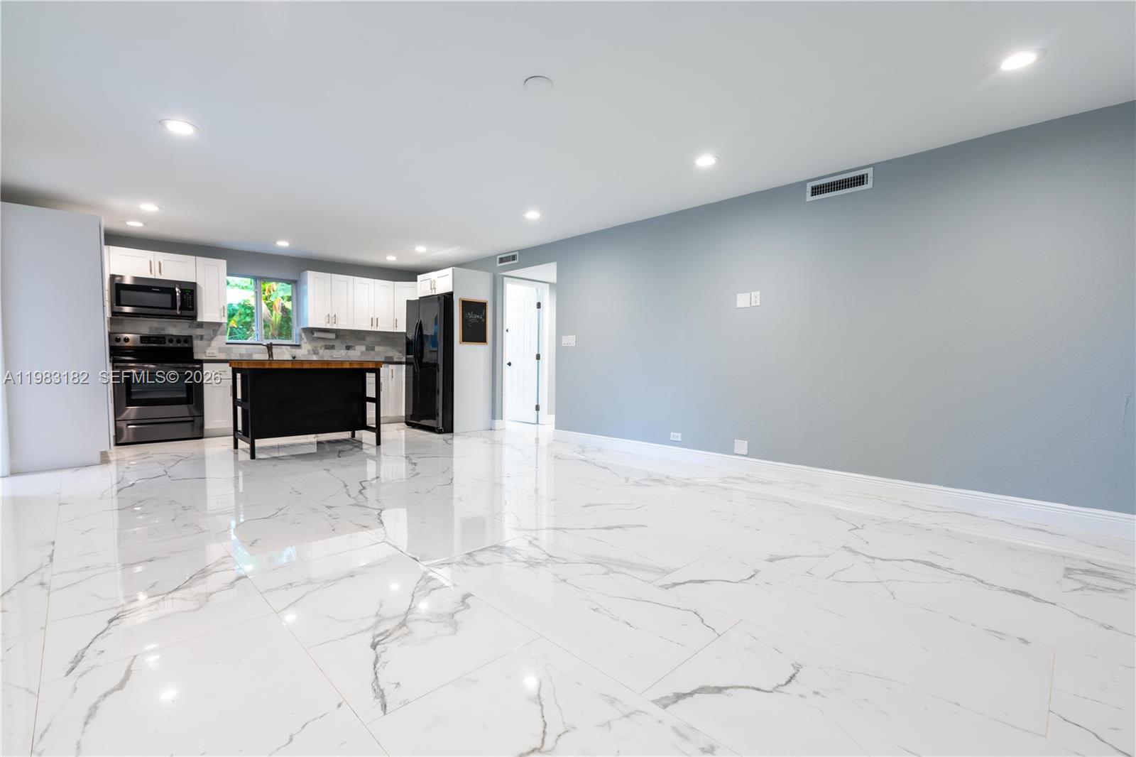 A kitchen with white cabinets and a black island opens into a spacious living area — 11 Judy Pl, Key Largo FL 33037, KEY LARGO, FL