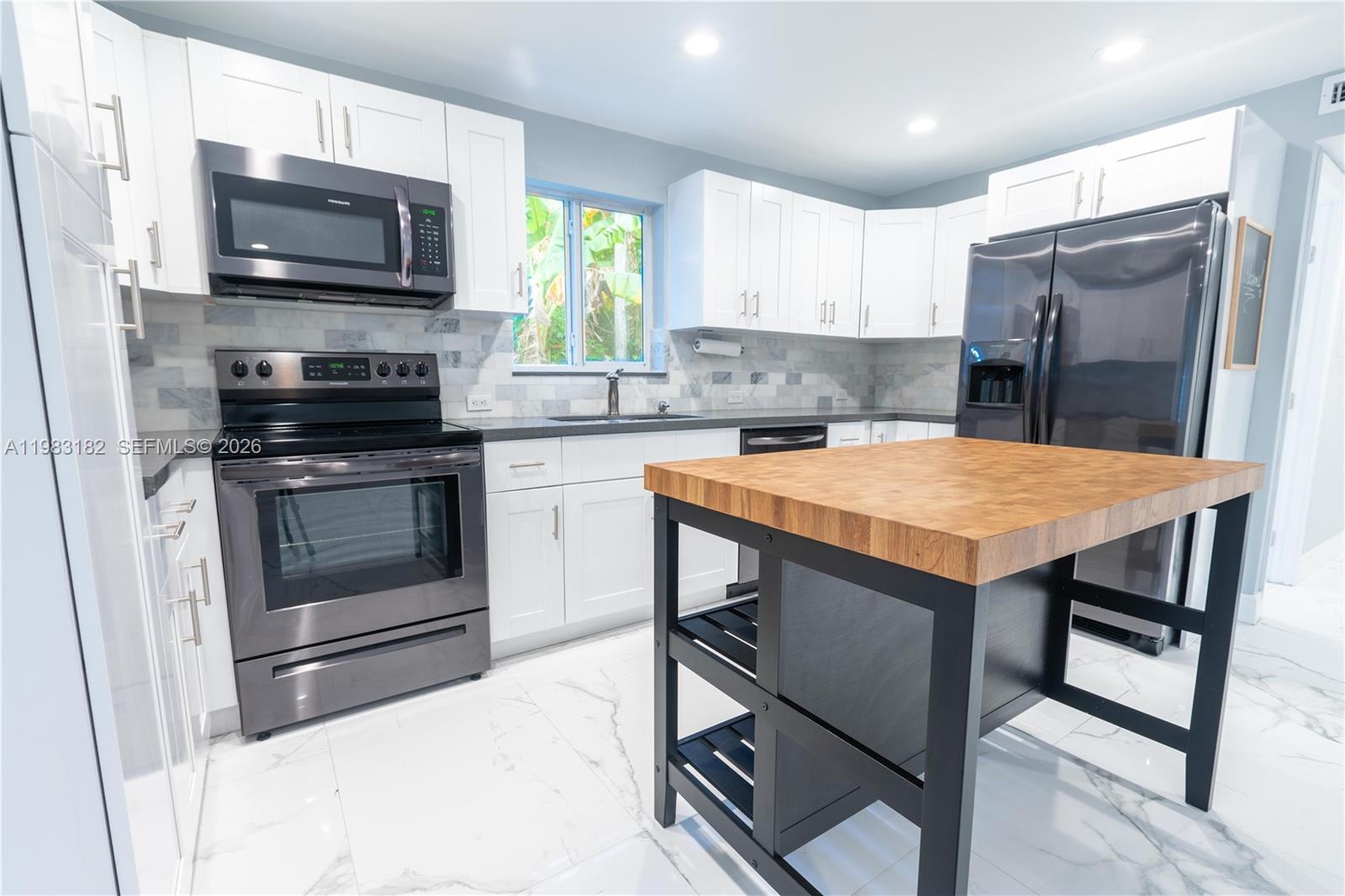 A modern kitchen features white cabinets, stainless steel appliances, a marble backsplash, and a wood-topped island — 11 Judy Pl, Key Largo FL 33037, KEY LARGO, FL