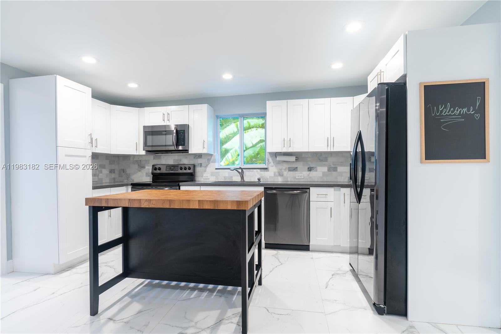 A modern kitchen features white cabinets, a black island with a wood top, and marble flooring — 11 Judy Pl, Key Largo FL 33037, KEY LARGO, FL