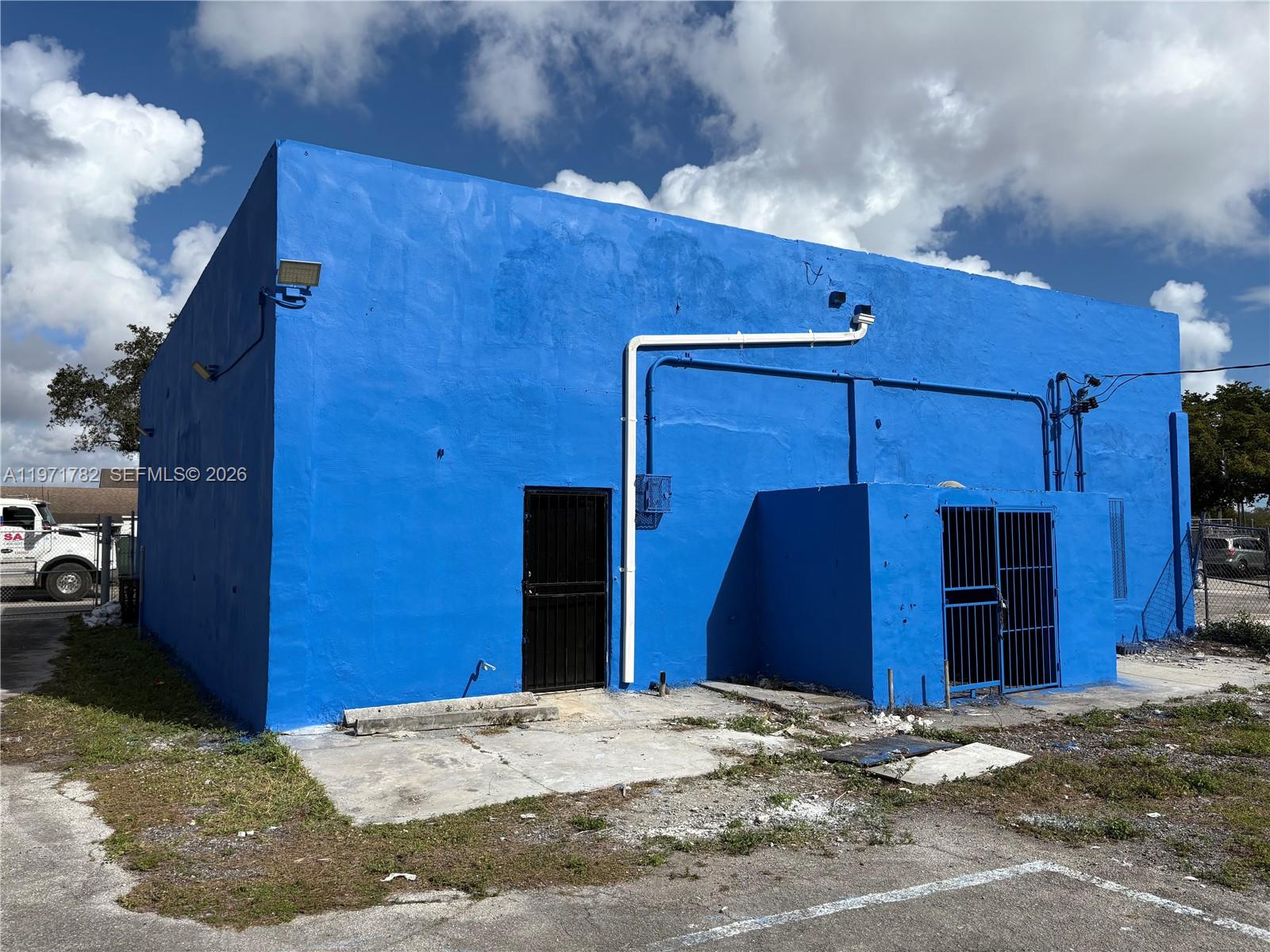 The exterior of a bright blue commercial building features a metal door and gated enclosure — 1350 NW 62nd St, Miami FL 33147, MIAMI, FL