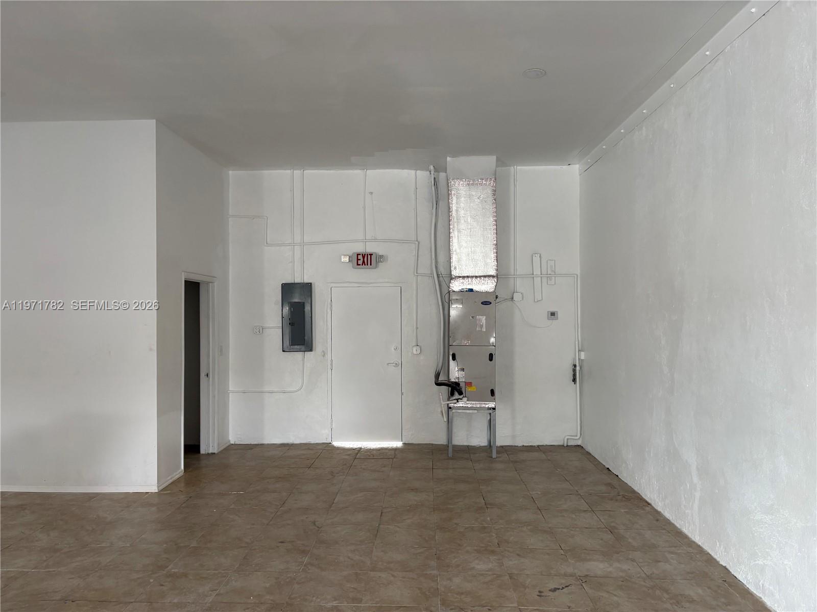 An empty commercial room features tiled floors, white walls, an exit door, and an HVAC unit — 1350 NW 62nd St, Miami FL 33147, MIAMI, FL