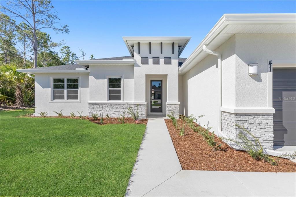 A modern single-story house exterior features white stucco walls, stone accents, and a glass-paneled door — 2235 SATURDAY STREET, NORTH PORT, FL