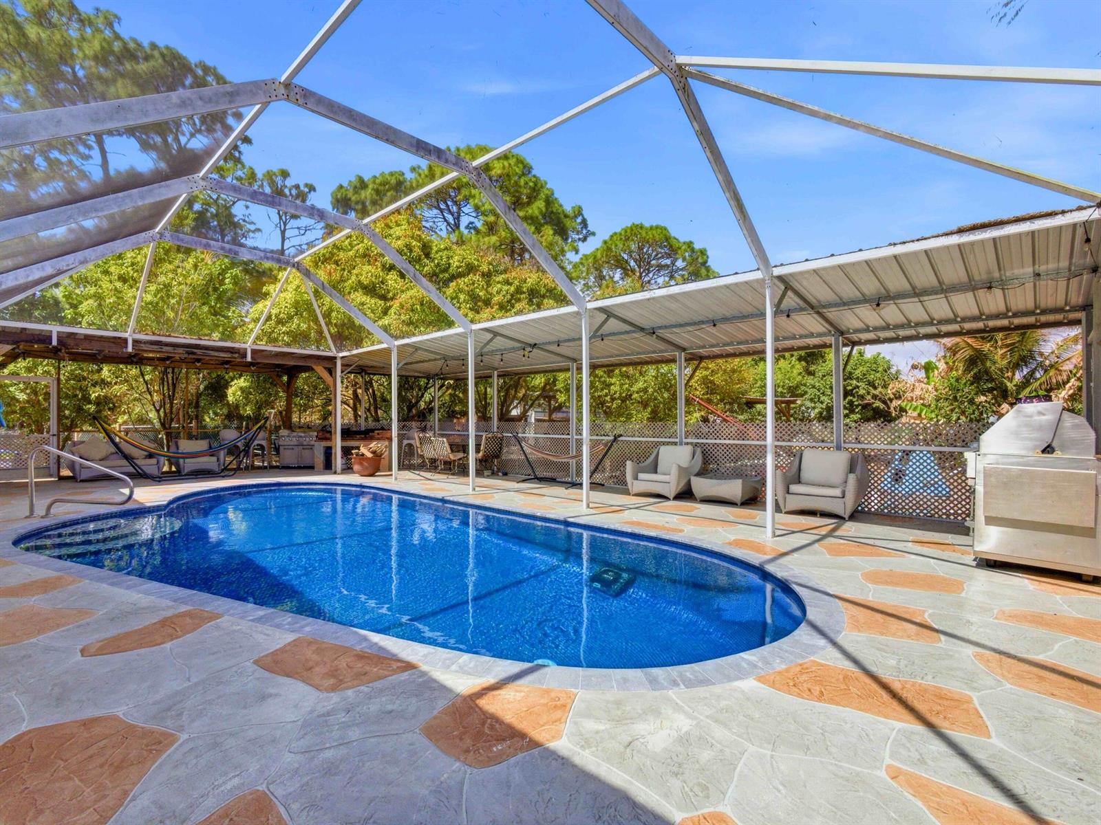A screened-in swimming pool area features a stone patio, outdoor seating, and a grill — 11481 Tangerine Boulevard, FL 33412, FL