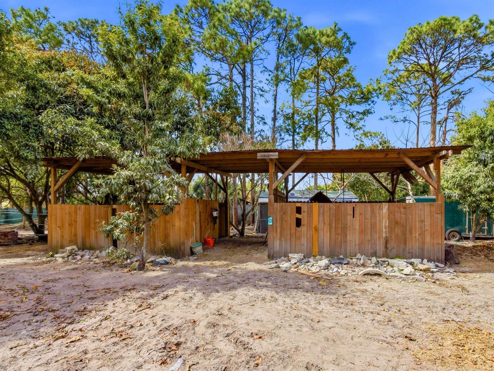 A wooden horse stable with a metal roof stands in a sandy, tree-lined outdoor area — 11481 Tangerine Boulevard, FL 33412, FL