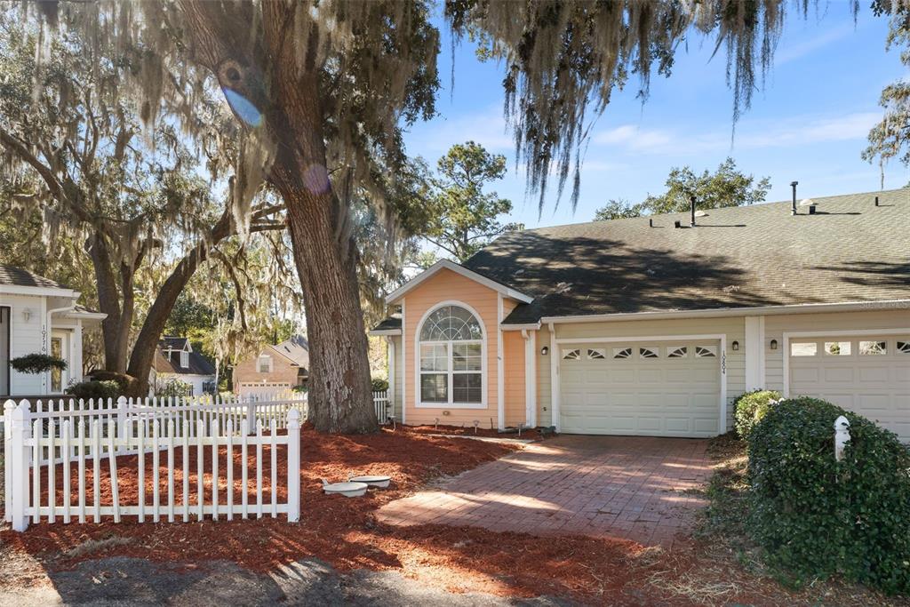 A peach-colored house with a brick driveway and a white picket fence under large trees — 10804 NW 65TH WAY, ALACHUA, FL