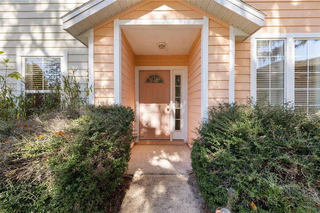 A peach-colored front door with a sidelight is framed by bushes and a covered porch — 10804 NW 65TH WAY, ALACHUA, FL