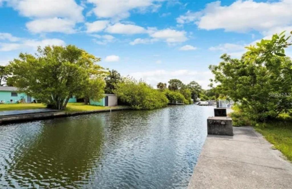 A concrete dock overlooks a narrow canal lined with lush green trees and residential homes — LOTS 13 & 14 SHEEPSHEAD DRIVE, HUDSON, FL