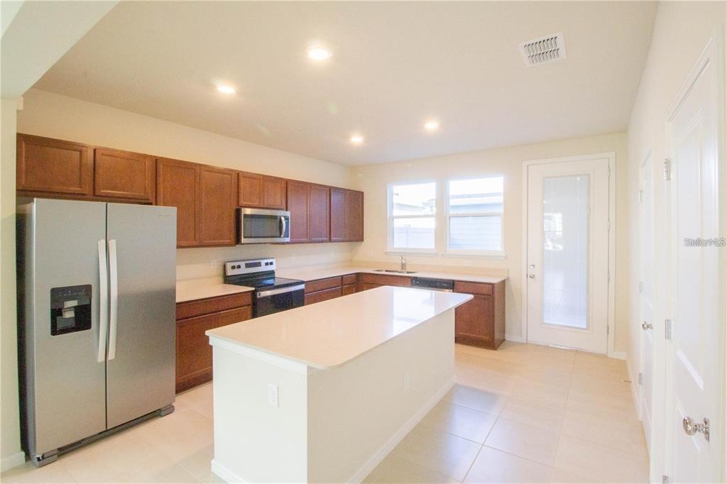 A kitchen features wood cabinets, stainless steel appliances, a center island, and light-colored countertops — 10355 FOLLY BEACH ROAD, ORLANDO, FL
