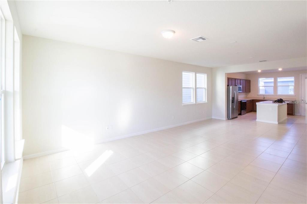 A bright, open-concept living area with light tile flooring leads into a kitchen with cabinets — 10355 FOLLY BEACH ROAD, ORLANDO, FL