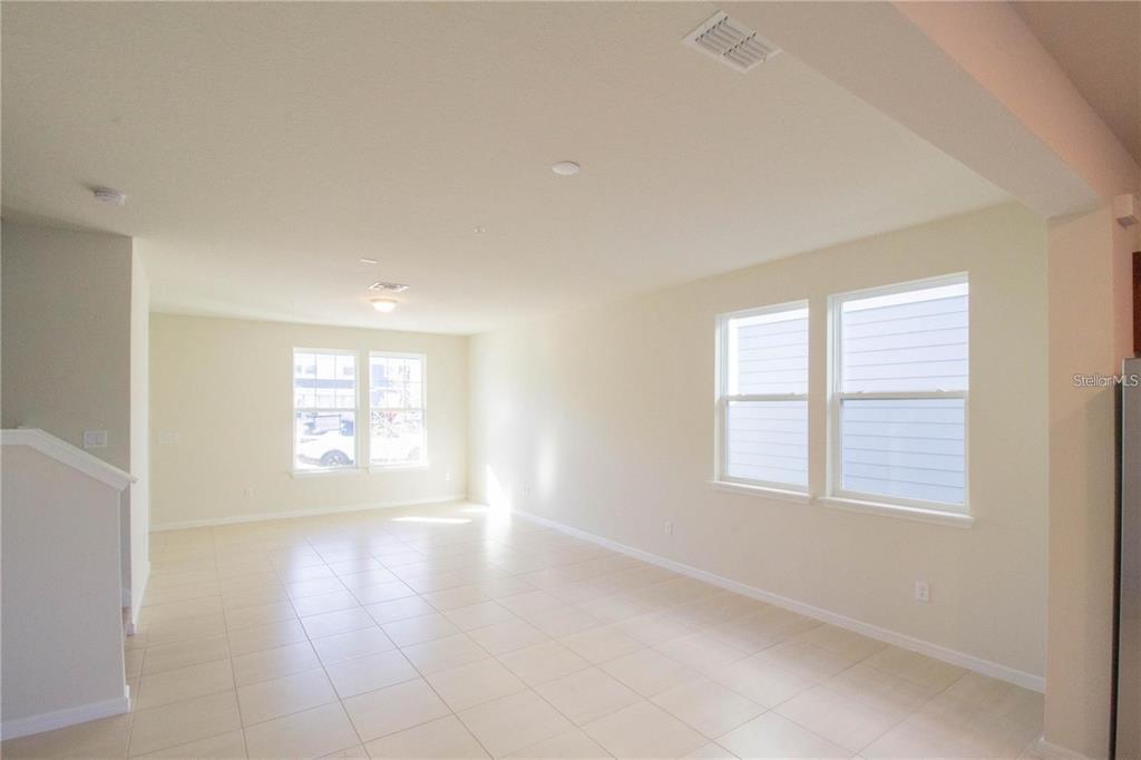 An empty room features light-colored tile flooring, neutral walls, and several windows — 10355 FOLLY BEACH ROAD, ORLANDO, FL