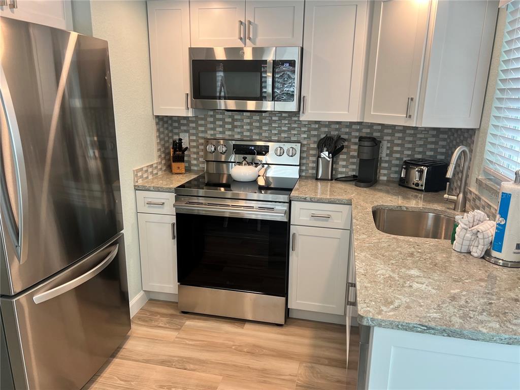 A kitchen with white cabinets, stainless steel appliances, and a gray stone countertop — 6154 MIDNIGHT PASS ROAD UNIT D16, SARASOTA, FL