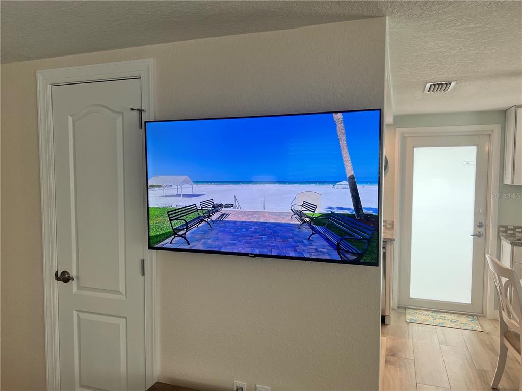A large flat-screen television is mounted on a wall next to a white door — 6154 MIDNIGHT PASS ROAD UNIT D16, SARASOTA, FL