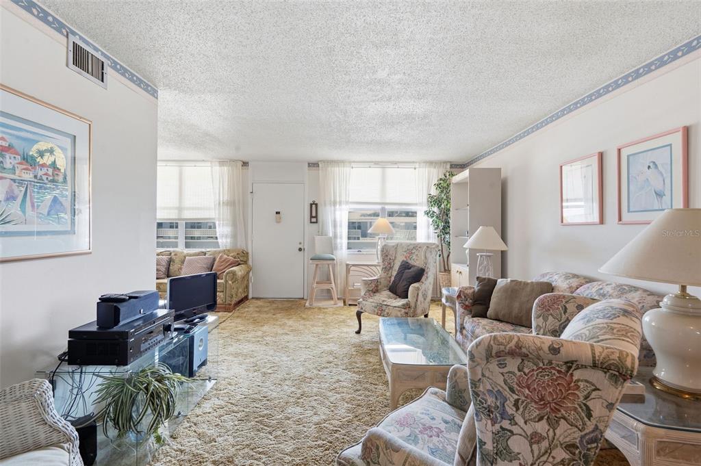 A living room features beige wall-to-wall carpeting, floral upholstered furniture, and a glass coffee table — 4890 BAY STREET NE UNIT 326, ST PETERSBURG, FL