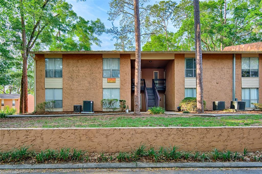 A two-story apartment building with tan stucco walls, dark wood stairs, and surrounding trees — 1810 NW 23RD BOULEVARD UNIT 188, GAINESVILLE, FL