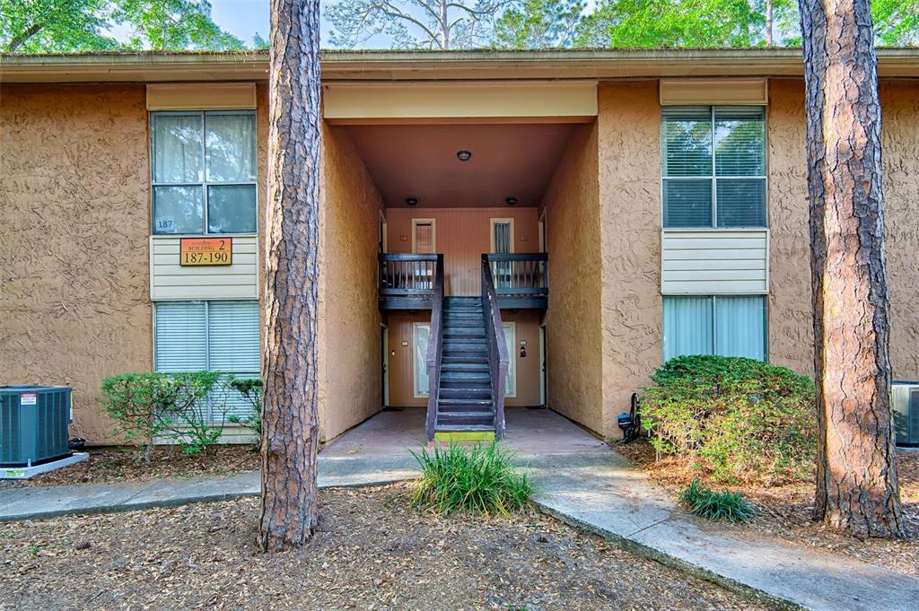 An exterior view of a two-story apartment building with a central staircase and pine trees — 1810 NW 23RD BOULEVARD UNIT 188, GAINESVILLE, FL