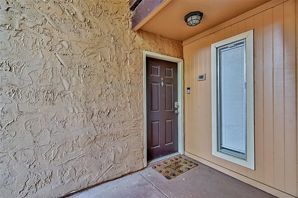An exterior view of a brown front door with a doormat and adjacent window — 1810 NW 23RD BOULEVARD UNIT 188, GAINESVILLE, FL