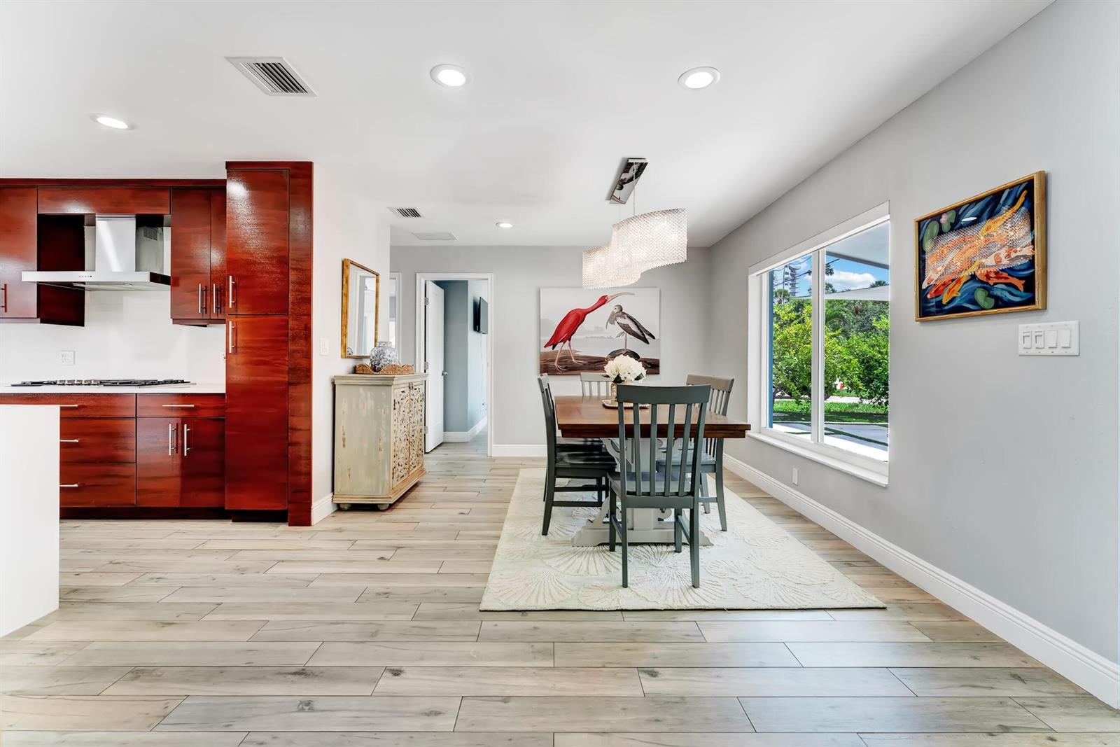 A dining area with a wooden table, grey chairs, and a modern chandelier near a kitchen — 2291 SE 15th Street, Pompano Beach FL 33062, POMPANO BEACH, FL