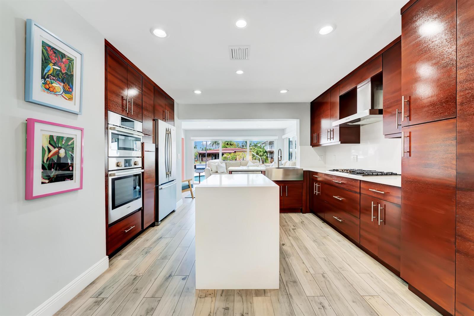A kitchen features dark wood cabinetry, a white central island, and light wood-look flooring — 2291 SE 15th Street, Pompano Beach FL 33062, POMPANO BEACH, FL