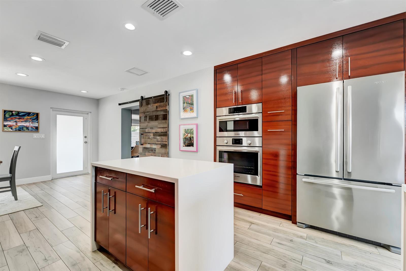 A modern kitchen features dark wood cabinetry, stainless steel appliances, a white island, and tile flooring — 2291 SE 15th Street, Pompano Beach FL 33062, POMPANO BEACH, FL