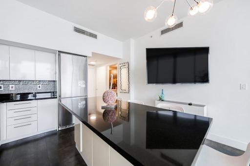A modern kitchen features white cabinetry, a black countertop island, and a wall-mounted television — 92 SW 3rd St # 5108, Miami FL 33130, MIAMI, FL