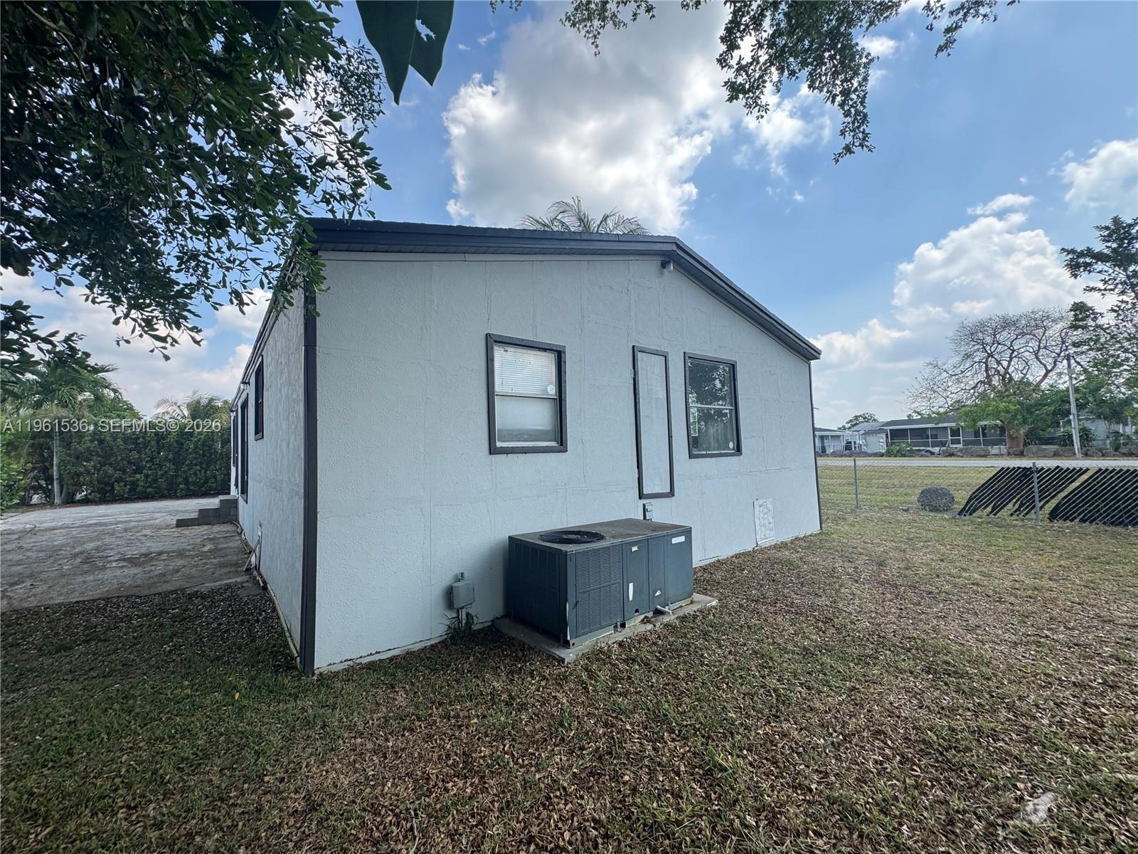 The exterior of a light-colored house features a central air conditioning unit and two windows — 19800 SW 180th Av #379, Miami FL 33187, MIAMI, FL