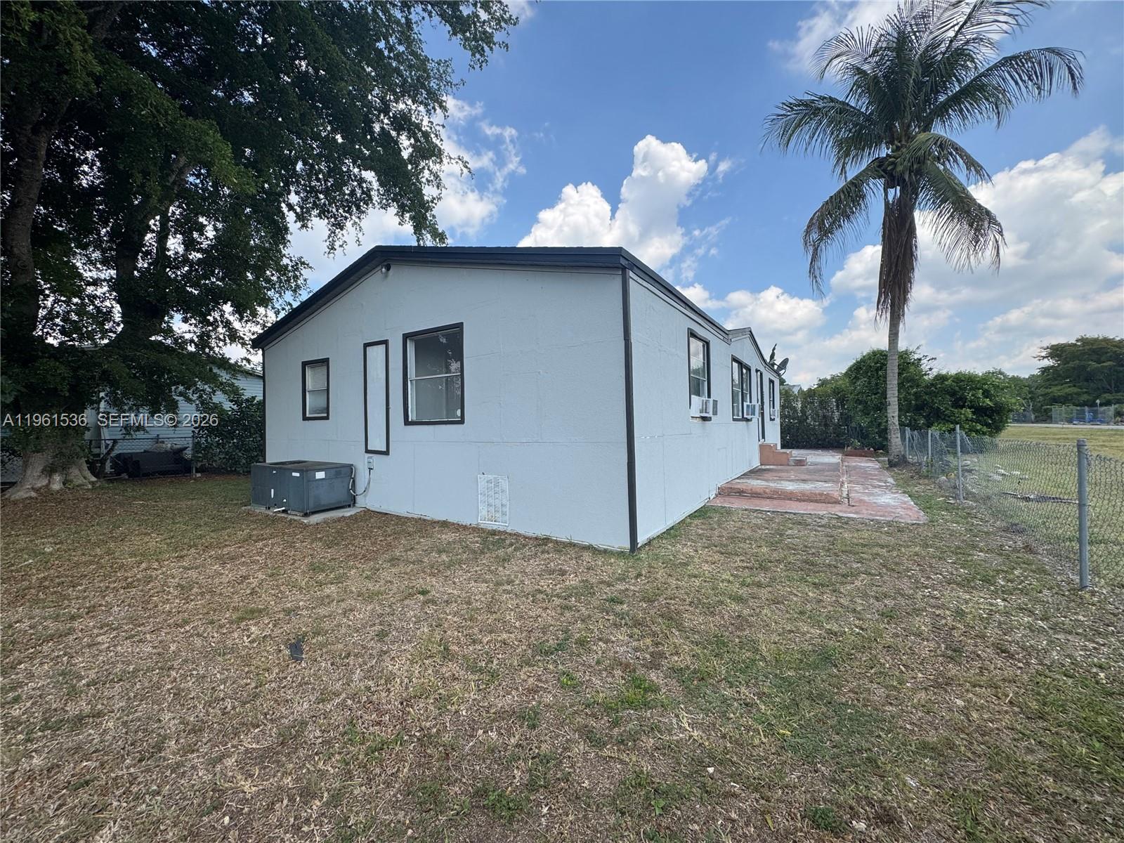 The exterior of a light-colored manufactured home features a palm tree and a fenced yard — 19800 SW 180th Av #379, Miami FL 33187, MIAMI, FL