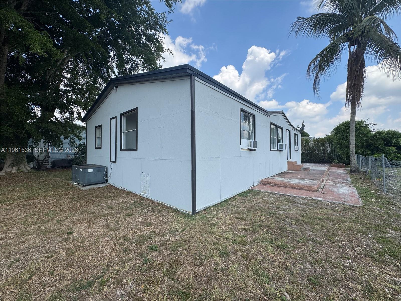 An exterior view of a light-colored mobile home with a concrete patio and palm tree — 19800 SW 180th Av #379, Miami FL 33187, MIAMI, FL