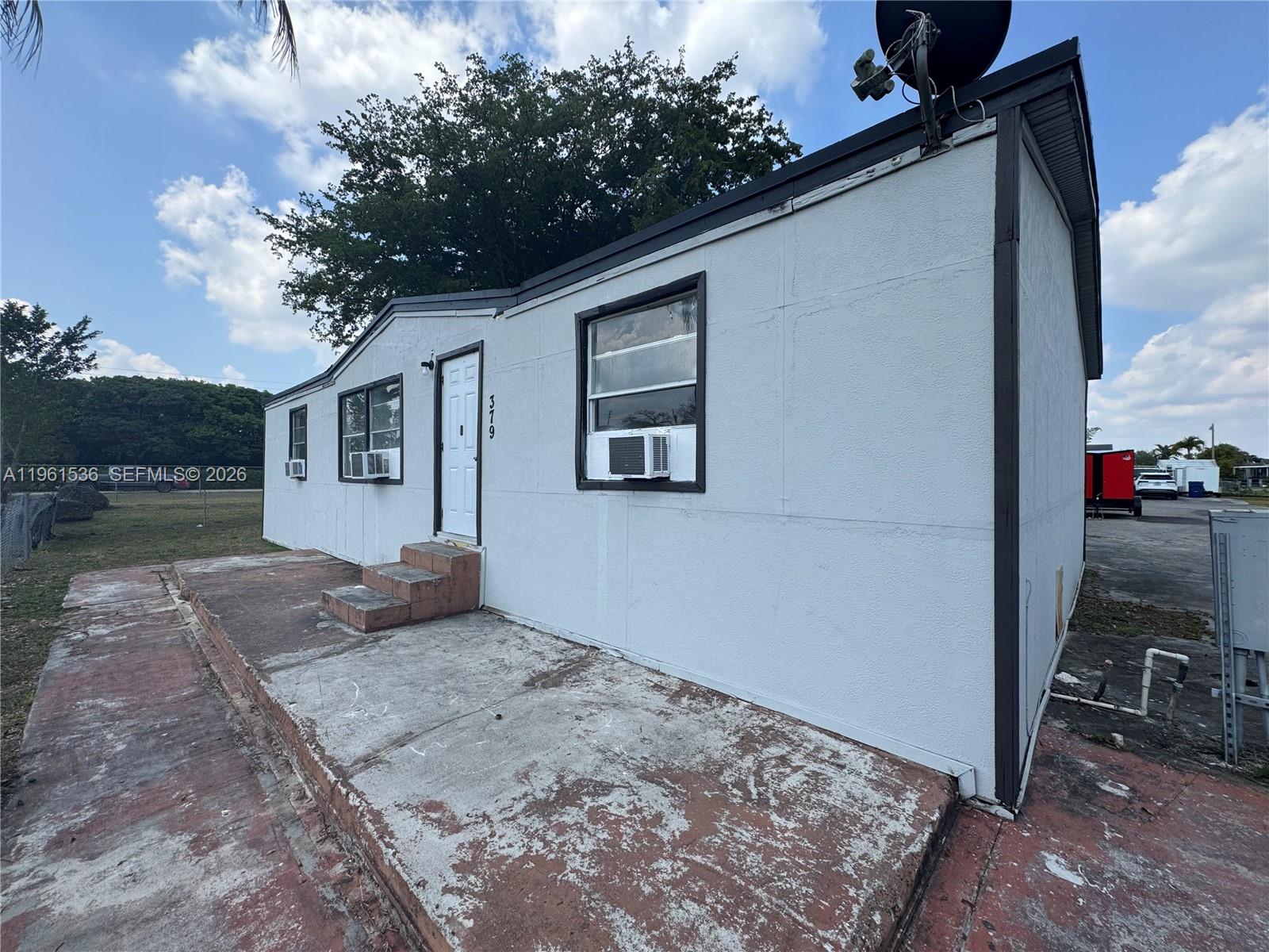 A single-story house with a concrete patio, window air conditioning units, and a white exterior — 19800 SW 180th Av #379, Miami FL 33187, MIAMI, FL
