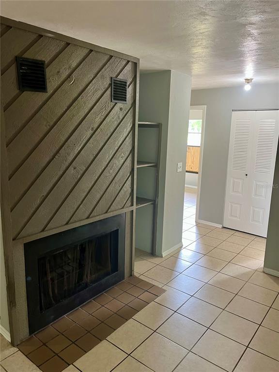 A room with a fireplace featuring diagonal wood paneling, tiled floors, and a white door — 2321 SW 31ST PLACE UNIT 1, GAINESVILLE, FL