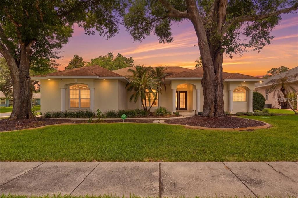 A single-story house with a light-colored stucco exterior, arched windows, and two large mature trees — 5237 BLOOMFIELD BOULEVARD, LAKELAND, FL